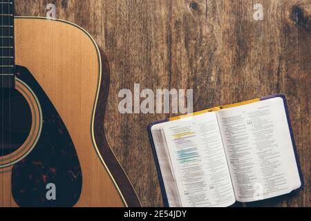 Una chitarra e una bibbia aperta su sfondo ligneo in un ambiente scarsamente illuminato. Luce soffusa e culto Foto Stock