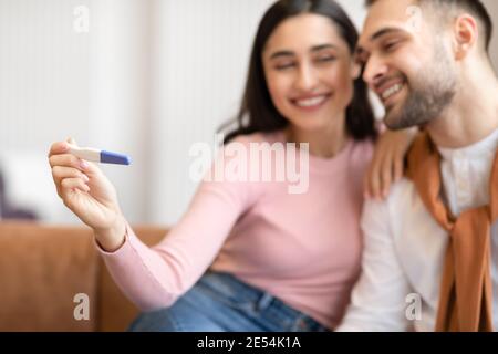 Gioiosa coppia araba che accanita a celebrare il test di gravidanza positivo seduto indoor Foto Stock