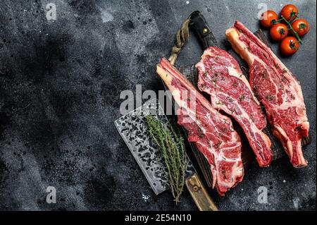 Assortimento di carni bovine a taglio crudo, bistecche all'osso. Sfondo nero. Vista dall'alto. Spazio di copia. Foto Stock