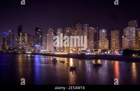 Splendida vista notturna dei grattacieli illuminati a dubai marina catturata dal ponte di pontile che collega Ain Dubai in isole di acqua blu Foto Stock