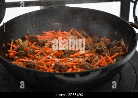 Primo piano di cottura del pilaf uzbeko nel calderone sul forno esterno. Carne, carote e cipolla. Cibo gustoso. Foto Stock
