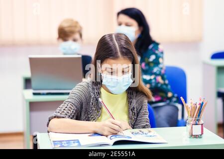 Bambini e insegnanti con maschera di protezione di ritorno a scuola in classe dopo il covid-19 blocco Foto Stock