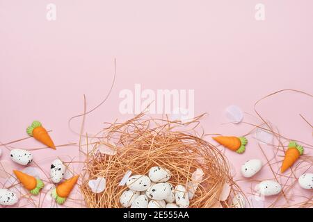 Uova di quaglia nel nido e carote dolci su sfondo rosa. Pasqua composizione orizzontale creativa minima con spazio di copia. Buona Pasqua di primavera Foto Stock