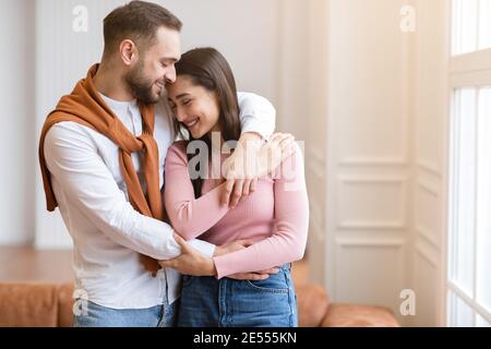 Il marito arabo amorevole abbracciando la giovane moglie che sta in piedi a casa Foto Stock