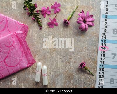 Protezione igienica della donna durante le mestruazioni. Tamponi in cotone, tamponi per mestruazioni rosa, fiori rosa e calendario di carta su tavola vintage. Spazio di copia. Foto Stock