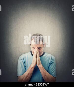 Uomo depresso di mezza età che prega su sfondo grigio parete con spazio copia sopra la testa. Uomo anziano disperato guardando verso il basso, tiene insieme le mani come pr Foto Stock