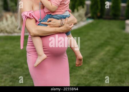 Immagine ritagliata di una donna incinta che coccola il suo bambino più grande. Donna in attesa che tiene il figlio in braccio e lo riposa sul suo urto di gravidanza. Foto Stock