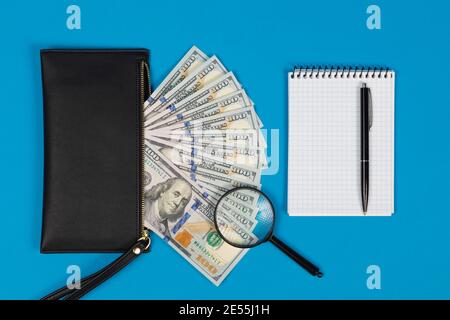 100 dollari USA fatture e lente d'ingrandimento con borsetta nera e blocco note. Concetto di denaro contraffatto Foto Stock