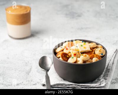 Mini pancake cereali e caffè dalgona su fondo grigio cemento, spazio copia. Cibo e bevande alla moda - minuscoli pancake serviti spruzzano e montato caffè istantaneo con latte o caffè coreano dalgona Foto Stock