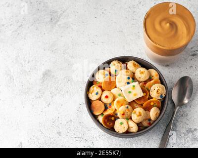 Mini frittelle cereali e caffè dalgona su sfondo grigio cemento spazio copia. Cibo e bevande alla moda - minuscoli pancake e caffè istantaneo montato con latte o caffè coreano dalgona. Vista dall'alto o piatta Foto Stock