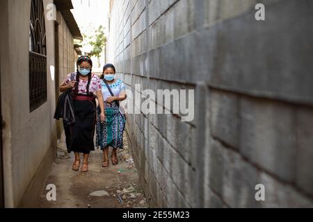 Le giovani donne camminano in un vicolo stretto indossando maschere facciali protettive a San Juan la Laguna, Guatemala, America Centrale. Foto Stock