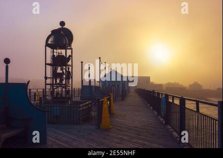 Orologio alimentato ad acqua sul molo di Southwold in un folto mare fret come il sole si rompe attraverso. Foto Stock