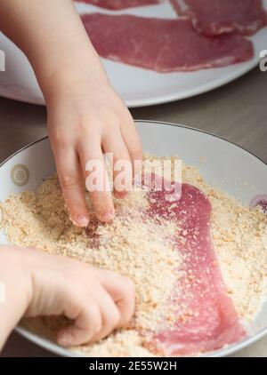 Bambino che copre carne di maiale con Breadcrumbs in cucina Foto Stock