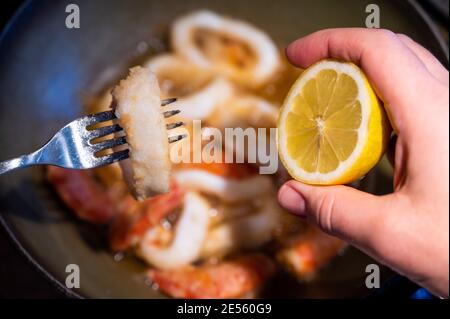 Scena di vita domestica: Sullo sfondo gamberetti infarinati e anelli di calamari fritti in olio bollente. In primo piano, un gamberetto sulla punta di una forchetta: il han Foto Stock