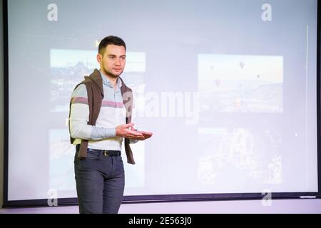 L'altoparlante maschio di successo conduce l'addestramento. Un uomo d'affari sta dando una lezione sullo sfondo di uno schermo bianco. Insegnante che dà una presentazione Foto Stock