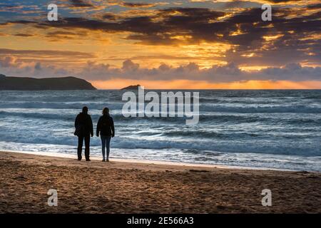 Una coppia che si erge sulla Fistral Beach, silhouette da uno spettacolare tramonto a Newquay in Cornovaglia. Foto Stock