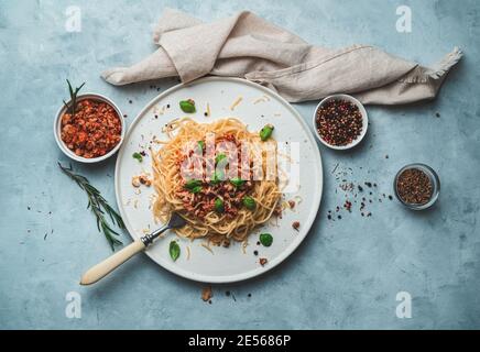 Piatto italiano, bolognese in piatto bianco piatto con condimento e tovagliolo beige su fondo grigio-blu. Foto Stock