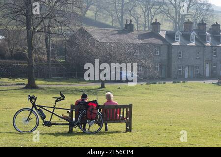 Una coppia si riposa dalla loro moto tandem su una panchina a Langcliffe, nello Yorkshire Dales. Foto Stock