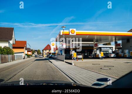 Schiltach, Germania - 7 ottobre 2018: Vista POV dalla macchina sulla grande lunga strada nel villaggio tedesco con distributore di benzina Shell sulla destra - cielo blu chiaro Foto Stock