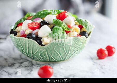 Insalata di pasta italiana con pomodori freschi, olive nere, polpette di mozzarella di cipolla rossa, basilico e condimento con olio d'oliva su tavola di marmo. Estremo Foto Stock