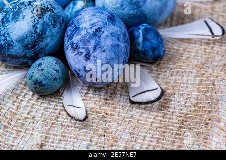 Uova di Pasqua blu sul burlap con piuma. Primo piano, messa a fuoco selettiva Foto Stock