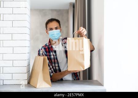 Addetto alla consegna con sacchetto di carta contenente cibo, addetto alla consegna degli alimenti in maschera protettiva Foto Stock