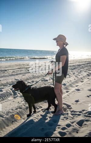 Una donna porta il suo nero labrador Retriever in spiaggia per la prima volta ad Atlantic Beach, North Carolina. Foto Stock