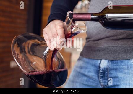 Primo piano sulla sezione centrale di un uomo caucasico sconosciuto che versa rosso vino in bottiglia nel decanter a casa in giornata Foto Stock