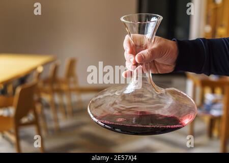 Primo piano a disposizione di un uomo caucasico sconosciuto che detiene il decanter con vino rosso nella sala a casa o al ristorante con spazio per la copia Foto Stock