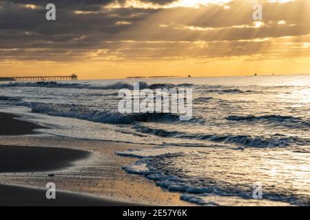 I raggi del sole brillano attraverso le nuvole all'alba ad Atlantic Beach, Carolina del Nord. La silhouette di un molo può essere vista all'orizzonte. Foto Stock