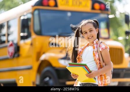 Bambina in piedi da una grande porta dell'autobus della scuola con il suo zaino. Foto Stock