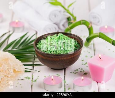 Centro benessere. Sale verde di spirulina a base di erbe in ciotola di ceramica, asciugamani termali, candela rosa profumata e bambù. Foto Stock