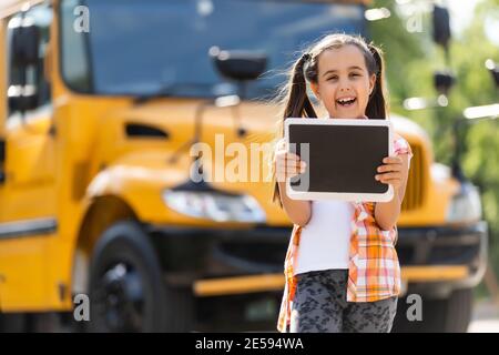 Bambina in piedi da una grande porta dell'autobus della scuola con il suo zaino. Foto Stock