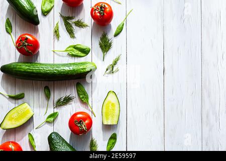 Pomodori, avocado, cetrioli, interi e a metà, foglie e aneto di spinaci, piatti giacono su una superficie di legno bianco. Concetto di cibo sano. Cibo sfondo. Foto Stock