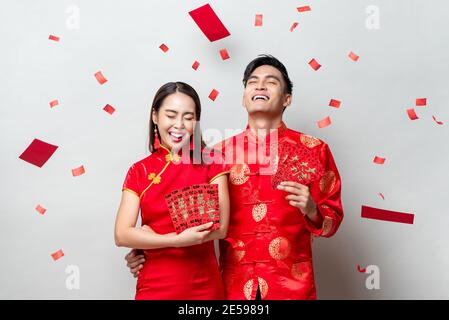 Felice coppia asiatica in costumi orientali tradizionali che tengono buste rosse o Ang Pao in grigio chiaro sfondo per i concetti cinesi nuovo anno, testi me Foto Stock