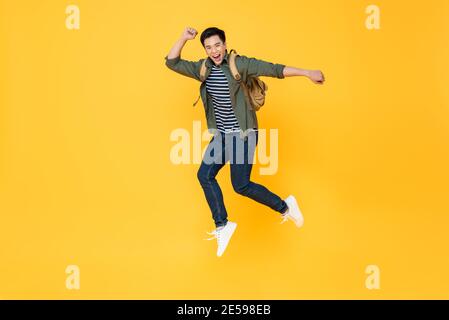 Felice sorridente giovane turista asiatico con zaino che salta dentro isolamento a mezz'aria su sfondo giallo Foto Stock