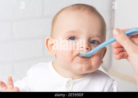 Madre che allatta il bambino con il cucchiaio blu del bambino. Prima purea di frutta del bambino. Primo piano foto del bambino caucasico. Bambino imparando a mangiare. Foto Stock