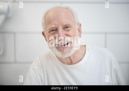 Uomo dai capelli grigi in camicia bianca ridendo vigorosamente Foto Stock