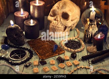Ancora vita con candele nere, cranio malvagio e rune su tavola di legno di strega. Sfondo esoterico, gotico e occulto, concetto mistico di Halloween. Foto Stock