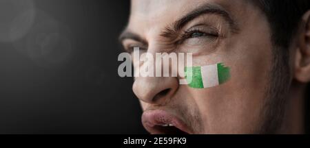 Un uomo urlante con l'immagine del nigeriano nazionale bandiera sul viso Foto Stock