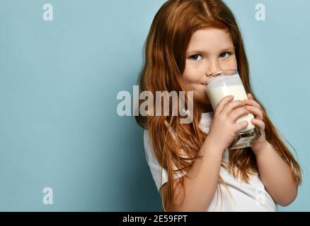 Ritratto di felice ragazza di capretto dai capelli rossi che beve latte o. yogurt su sfondo blu con spazio libero per la copia Foto Stock