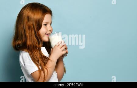 Felice ragazza di capretto dai capelli rossi si leva di lato alla macchina fotografica che tiene un bicchiere di latte o di yogurt che beve guardando la copia gratuita spazio Foto Stock