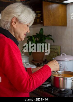 Donna in maglione rosso che prepara zuppa in cucina. Donna a fuoco selettivo in pullover rosso. Tradizionale tarhana di sapone turco. Foto Stock