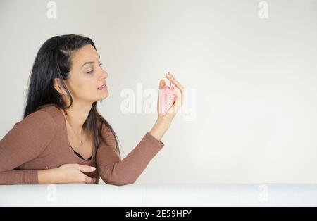 donna che tiene un cuore in mano, seduto sul divano di fronte al muro bianco bkank. Foto Stock