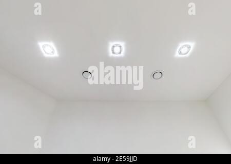 soffitto sospeso con lampade alogene spot e costruzione di cartongesso in camera vuota in appartamento o casa. Soffitto elasticizzato bianco e forma complessa. Foto Stock