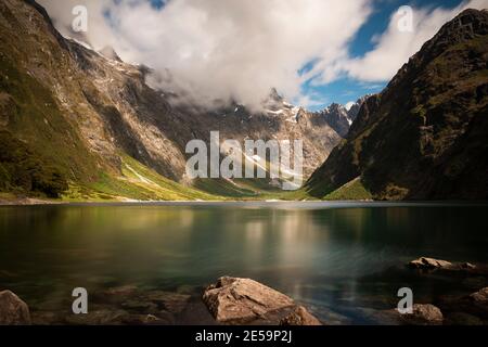 Il lago Marian, con le nuvole basse, getta ombre sulla valle profonda, Fiordland National Park, Nuova Zelanda Foto Stock