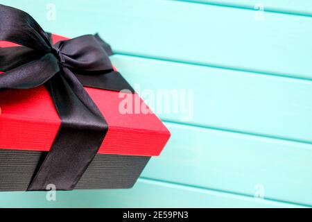 La scatola rossa è legata da un ampio nastro nero. Regalo su sfondo blu. Foto Stock