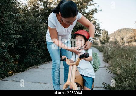 Madre che aiuta il suo bambino a fissare un casco da bicicletta. Donna e bambino su una bicicletta che indossa un casco. Foto Stock