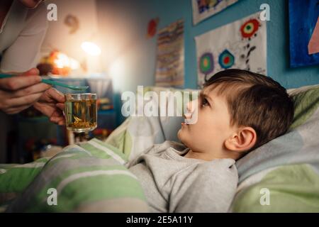 Un bambino malato che si trova a letto nella sua stanza rifiutandosi di prendere un medicinale. Un ragazzo non disposto a prendere una medicina da sua madre. Foto Stock