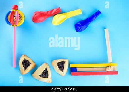 Hamantaschen biscotti o amans orecchie, legno colorato noisemakers e palloncini per Purim celebrazione ebraico carnevale vacanza su sfondo blu.Top view.Flat Lay. Spazio di copia. Foto Stock